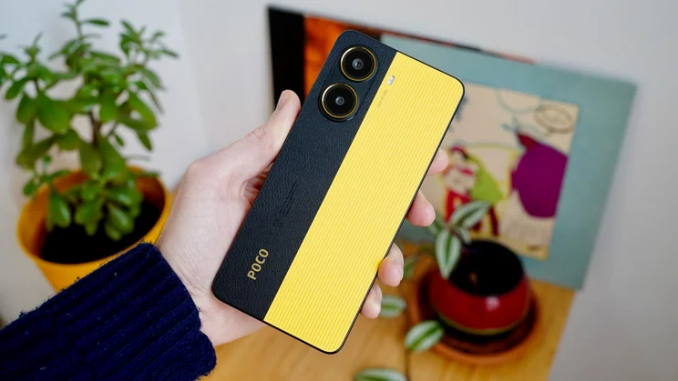 Xiaomi Poco X7 Pro in hand, rear view, in front of a table laden with potted plants