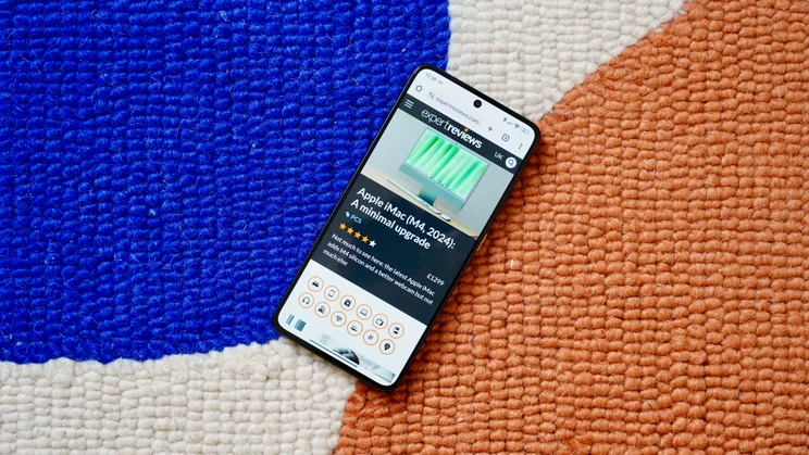 Xiaomi Poco X7 Pro on a multi-coloured rug, display showing the Expert Reviews homepage