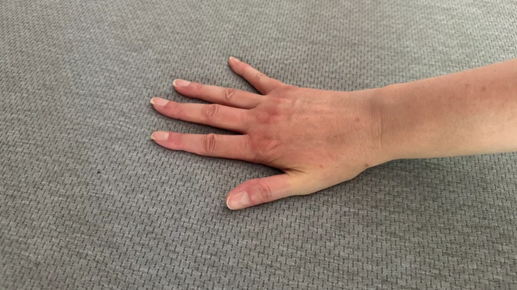 A hand pushing down on the surface of the Zoma Hybrid mattress