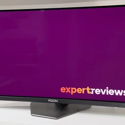 The AOC Agon Pro AG276QZD2 monitor on a white desk, pictured from an angle, showing the Expert Reviews logo on screen