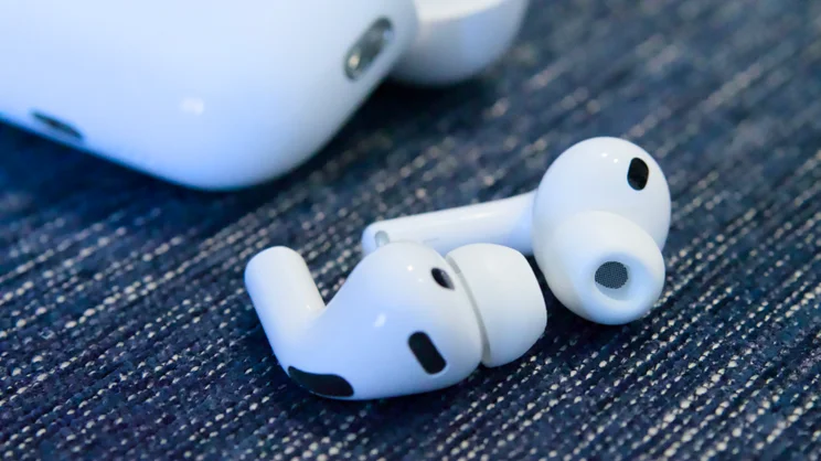 The Apple AirPods Pro 3 earbuds shown in close up with the charging case in the background