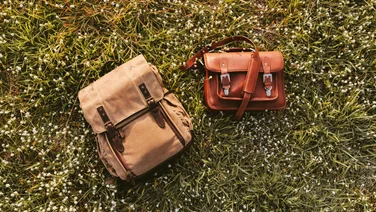 A backpack and a messenger bag are placed next to each other in a field