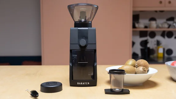The Baratza Encore ESP Pro coffee grinder on a kitchen surface, alongside its accessories and a bowl of kiwis
