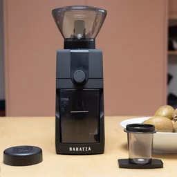 The Baratza Encore ESP Pro coffee grinder on a kitchen surface, alongside its accessories and a bowl of kiwis