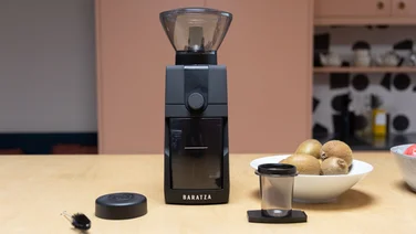 The Baratza Encore ESP Pro coffee grinder on a kitchen surface, alongside its accessories and a bowl of kiwis