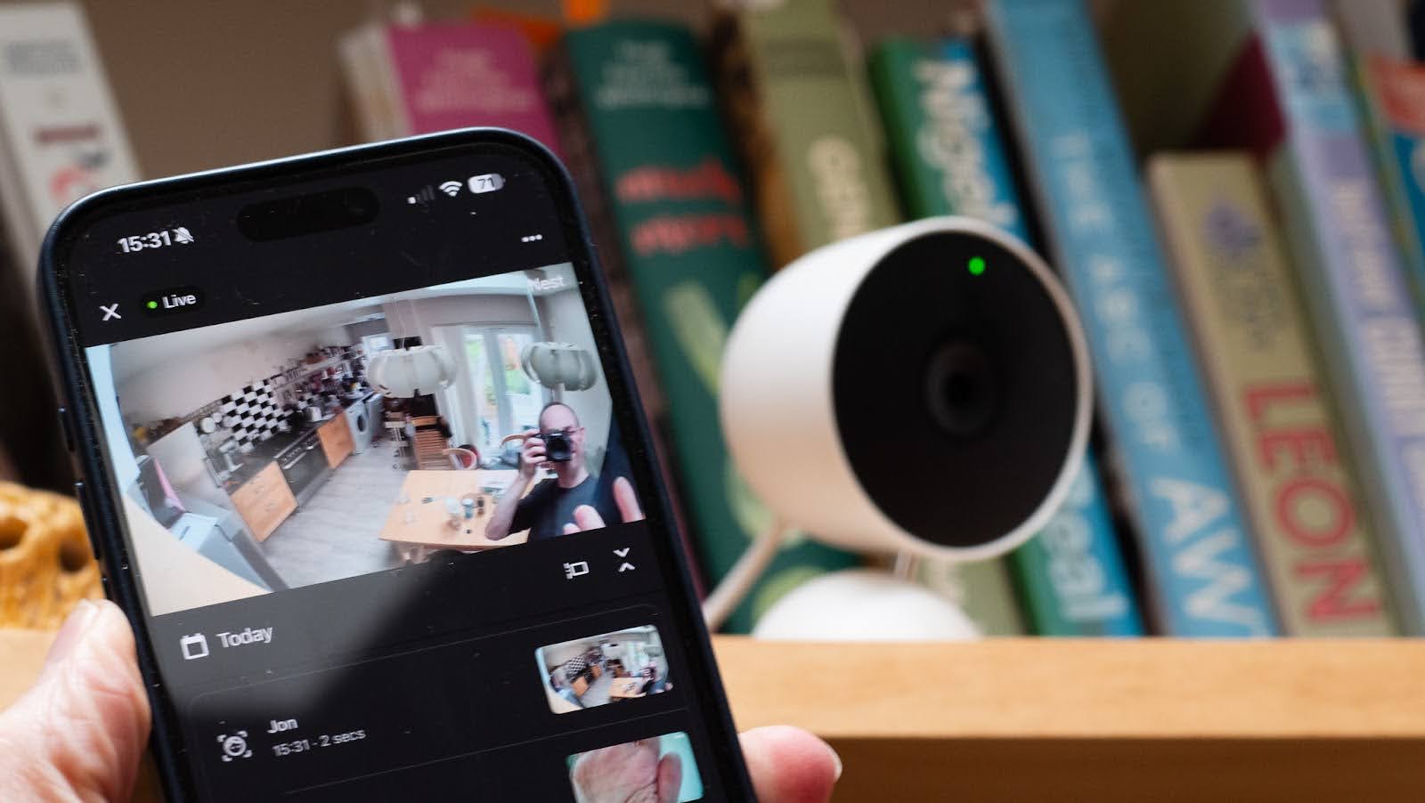 Best home security camera. The view from an indoor camera on a phone screen in front of the Nest Cam Indoor standing on a bookshelf 