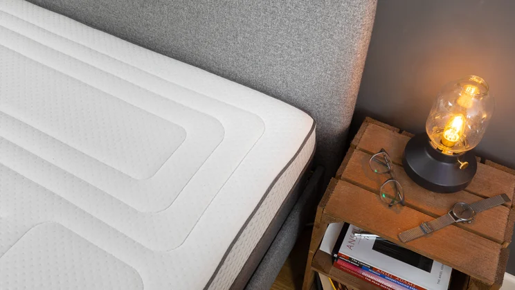 A hybrid mattress next to a bedside table with a lamp and books