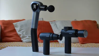 Best massage gun - Three massage guns lined up on a white table in front of a sofa