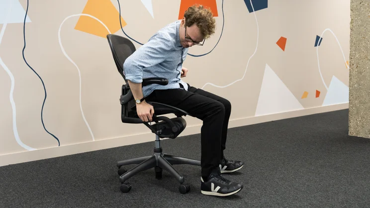 A person sitting on the Herman Miller Aeron office chair in an office. They are adjusting the height setting.