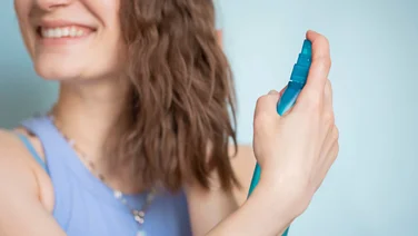 A smiling woman sprays her hair with a Sea Salt spray