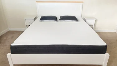 A mattress with two pillows on a white bed frame