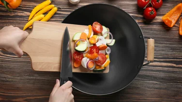 Chopped vegetables being swept from a chopping board into a frying pan