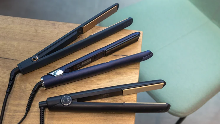 best hair straighteners an image of three hair straighteners arranged on a wooden vanity table next to a green fabric chair