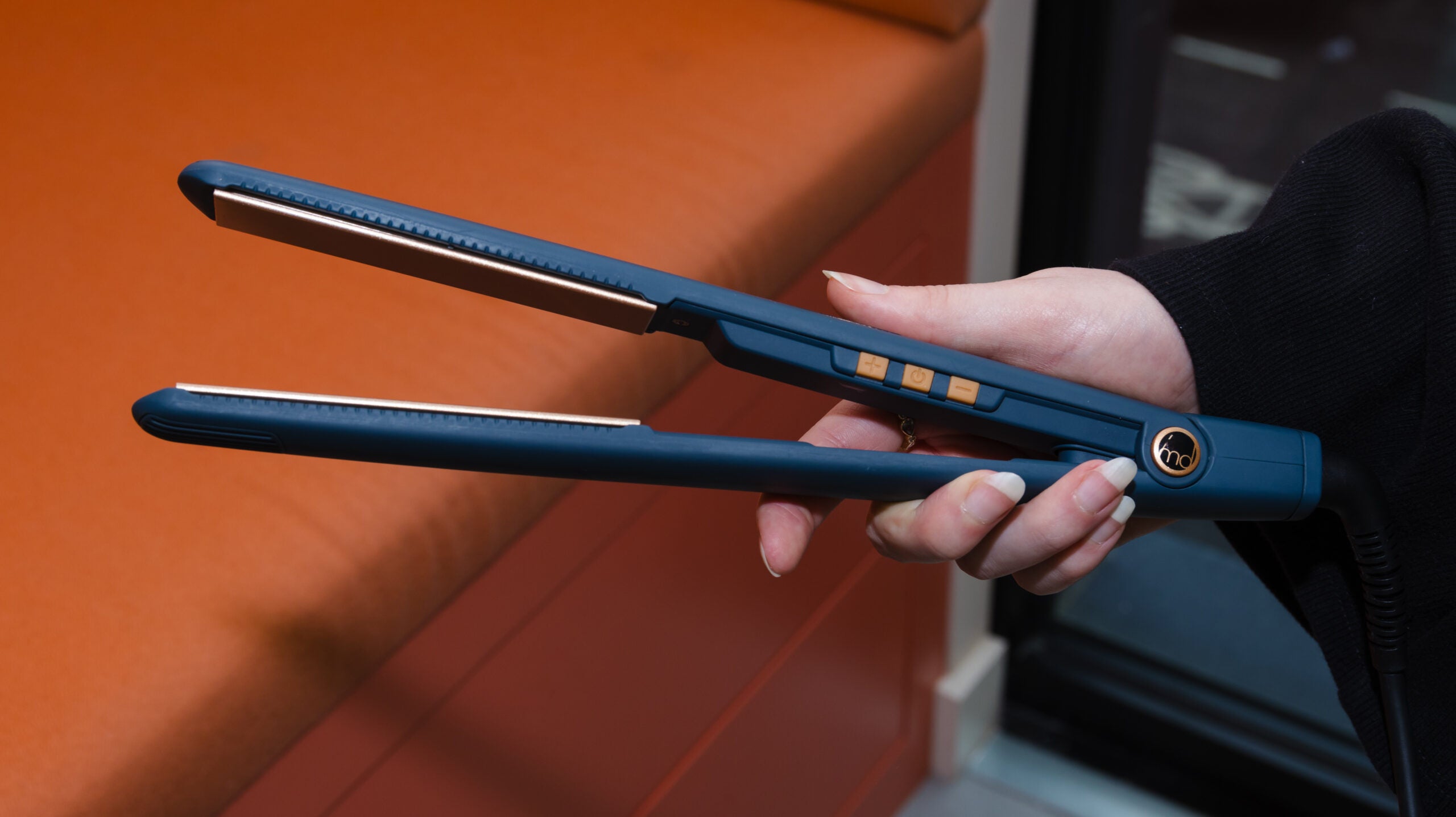 best hair straightener an image showing how we test hair straighteners. Woman's hand holding the straighteners in front of an orange background