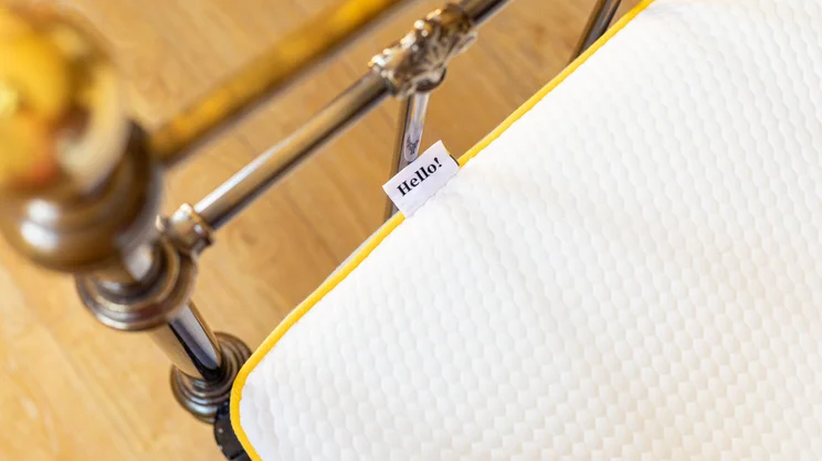 Corner of mattress with brass bed frame a "hello" tag