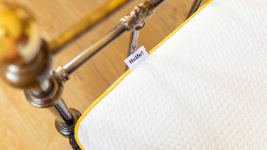 Corner of mattress with brass bed frame a "hello" tag