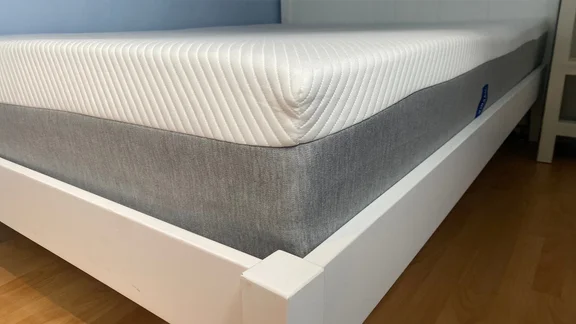 The corner of a mattress on a white bed frame