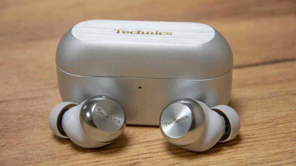 The Technics EAH-AZ100 true wireless earbuds outside of their charging case on a wooden table