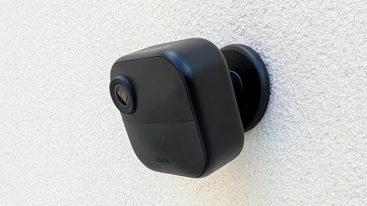 The Blink Outdoor 4 camera mounted on its bracket on a white wall
