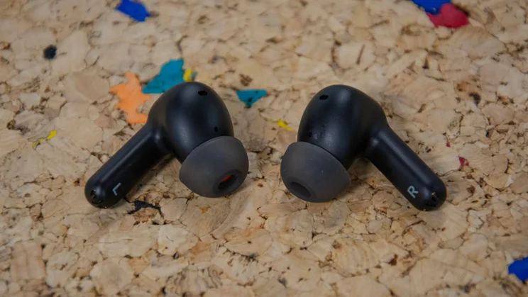 The Cambridge Audio Melomania A100 wireless earbuds on a cork table with their stems pointed outwards