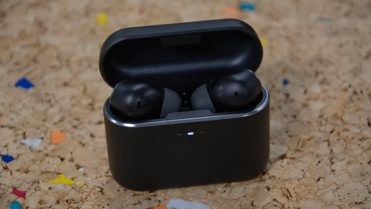The Cambridge Audio Melomania A100 wireless earbuds in their open charging case on a cork table