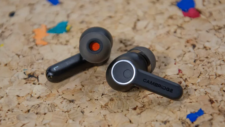 The Cambridge Audio Melomania A100 wireless earbuds on a cork table with one eartip turned upwards and the other showing the touch control panel