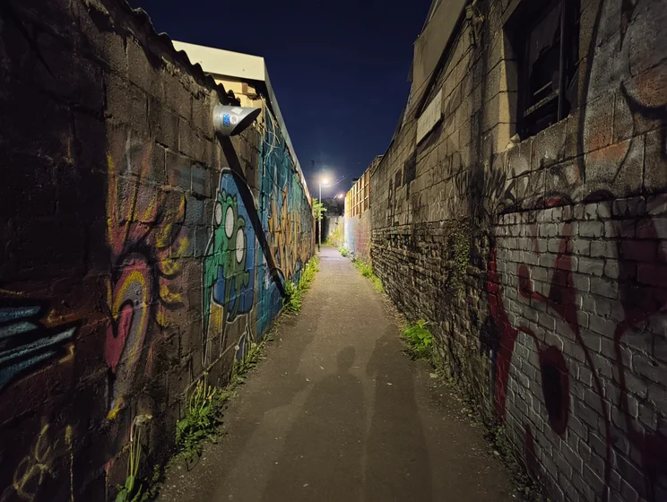 A dark alleyway at night, graffiti covering walls on both sides