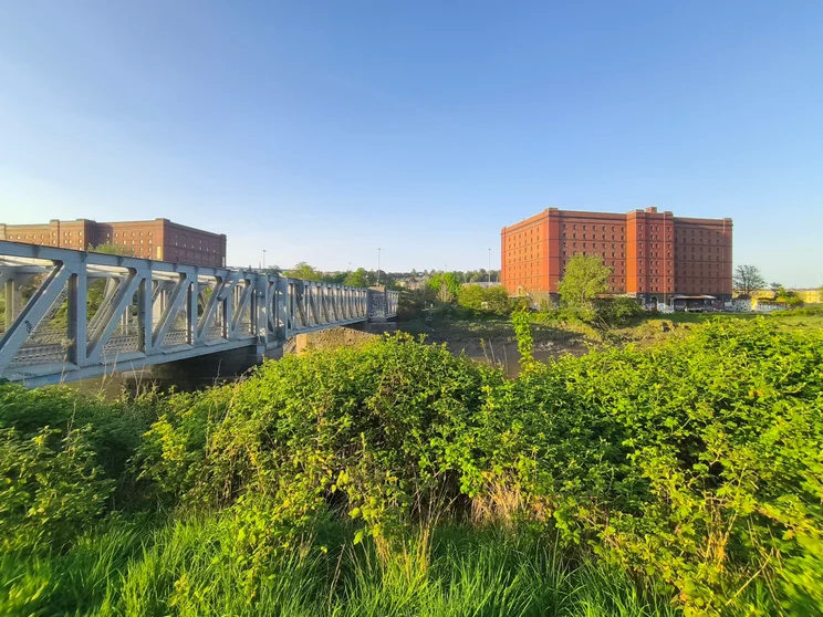 Wide-angle shot of a bridge crossing a river, with orange buildings on the far shore