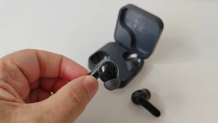 Our reviewer holding the left CMF Buds 2 wireless earbud in his hand with the other bud and charging case in the background