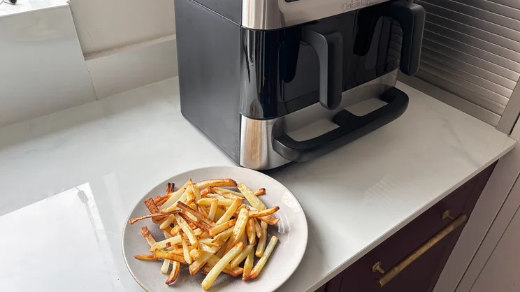 A plate of cooked chips in front of the Cuisinart Tri Zone 13.6l Air Fryer & Oven, on a kitchen worktop