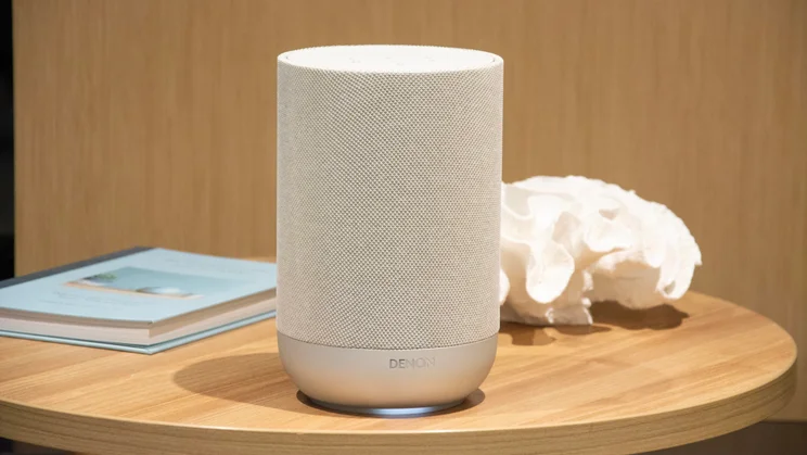 The Denon Home 200 wireless speaker on a table alongside a book and an ornament
