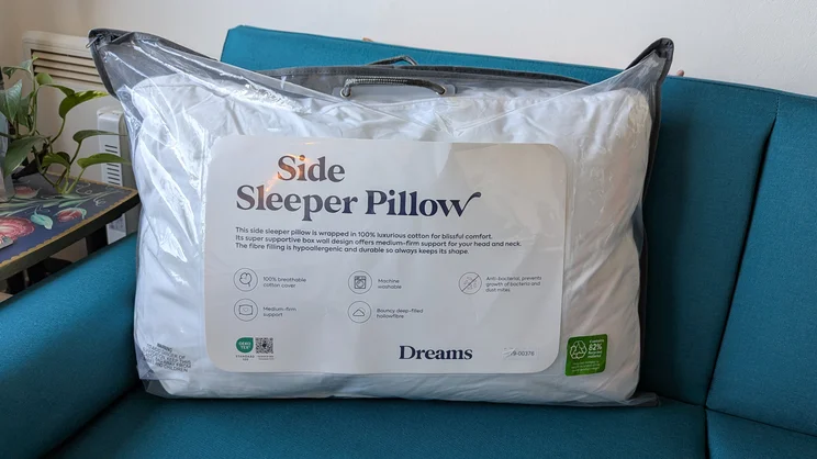 The Dreams Side Sleeper Pillow, in its bag, propped up on a blue sofa
