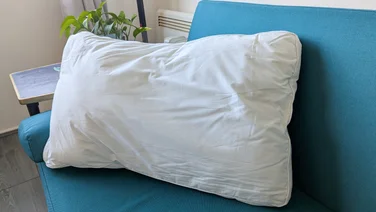 The Dreams Side Sleeper Pillow propped up on a blue sofa in a living room