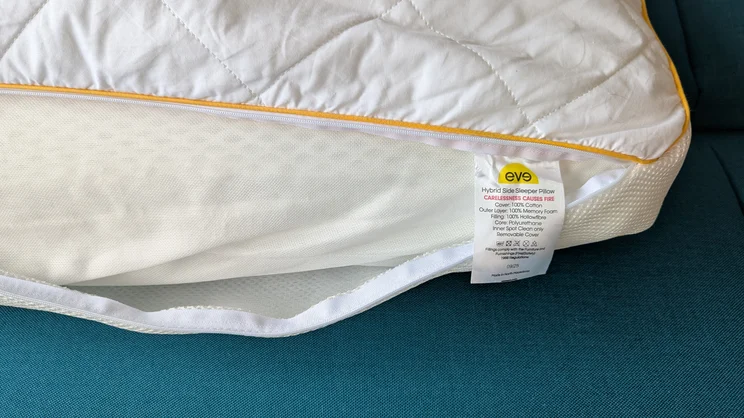 A corner of the Eve Hybrid Side Sleeper pillow. The cover is unzipped to show the pillow's inside and care label