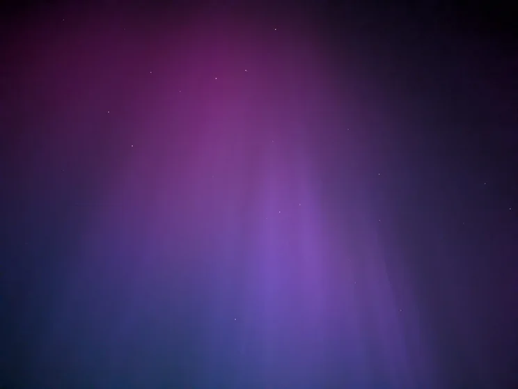 Purple and blue auroras in the sky with stars and planets shining through