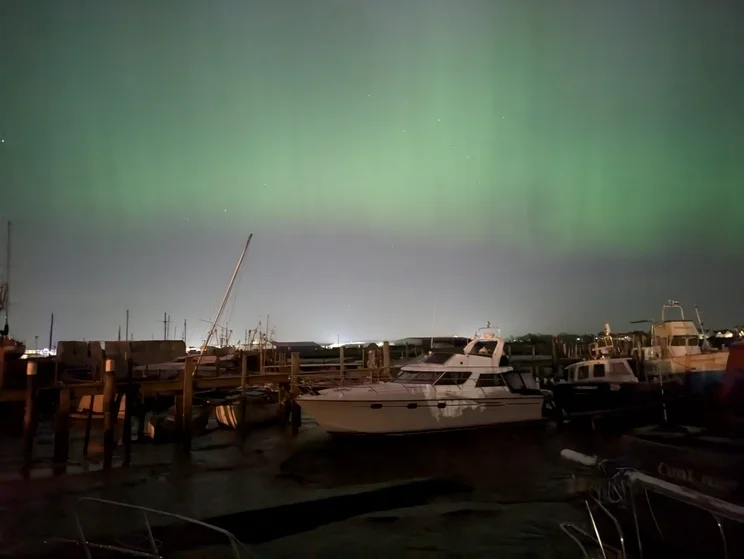 A dock at night with a green aurora borealis in the sky above