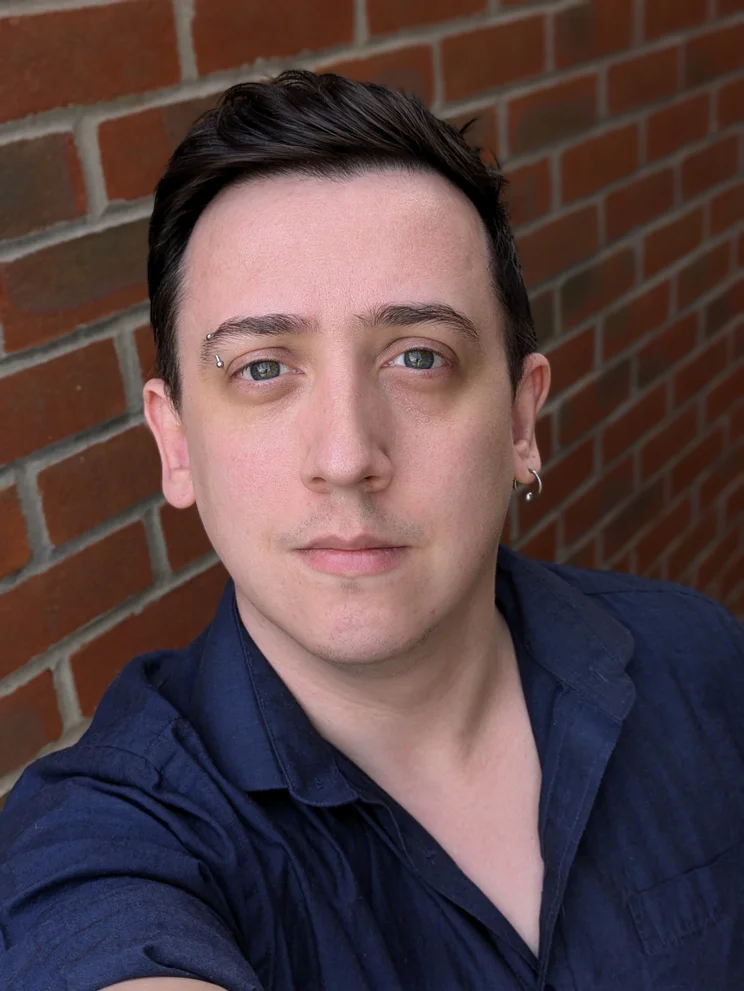 Portrait photo of a man in a blue shirt against a red brick wall