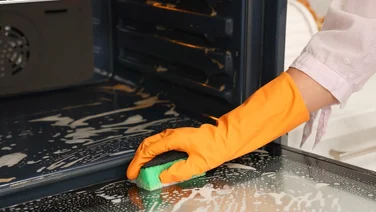 How to clean an oven woman with orange rubber gloves cleaning the oven door with a sponge
