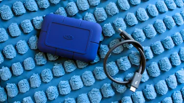The LaCie Rugged SSD Pro5 external hard disk, pictured with its Thunderbolt 5 cable on a blue Ikea cushion