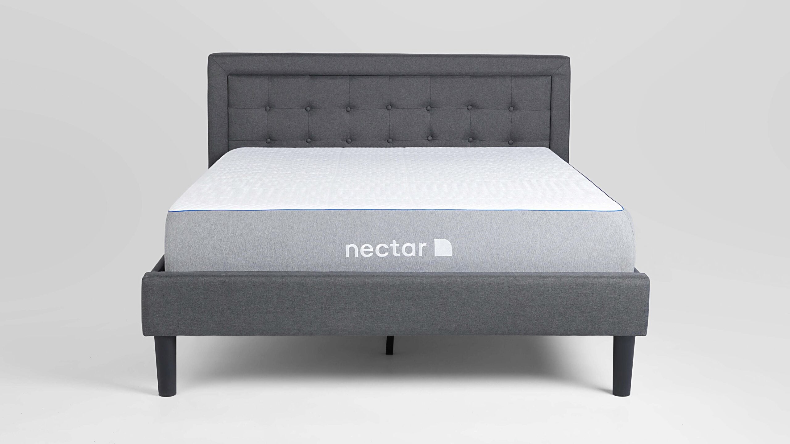 nectar essential hybrid mattress on an upholstered bed frame, on a grey background