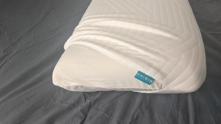 The Origin Coolmax Latex pillow with cover unzipped and partially removed, on a mattress
