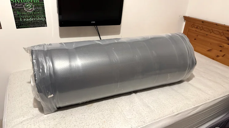 The Origin LumbarCloud mattress rolled up and vacuum sealed on a bed