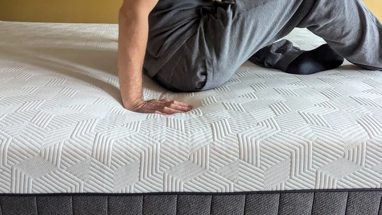A person sitting on the Panda Hybrid Bamboo mattress, pushing their hand into the mattress