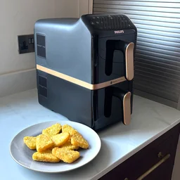 The Philips 4000 Series Stacked Dual Basket Air Fryer on a kitchen worktop, alongside a plate of cooked hash browns
