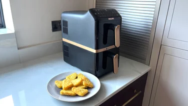 The Philips 4000 Series Stacked Dual Basket Air Fryer on a kitchen worktop, alongside a plate of cooked hash browns