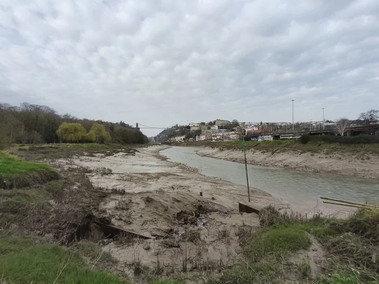 Wide-angle shot of a river at low tide with a bridge in the distance