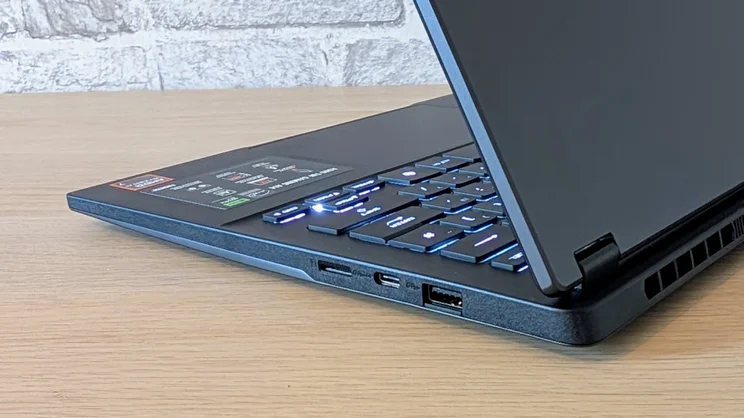 The Asus TUF Gaming A14 RTX 5060 laptop pictured from the rear right corner, half open, on a wood desk