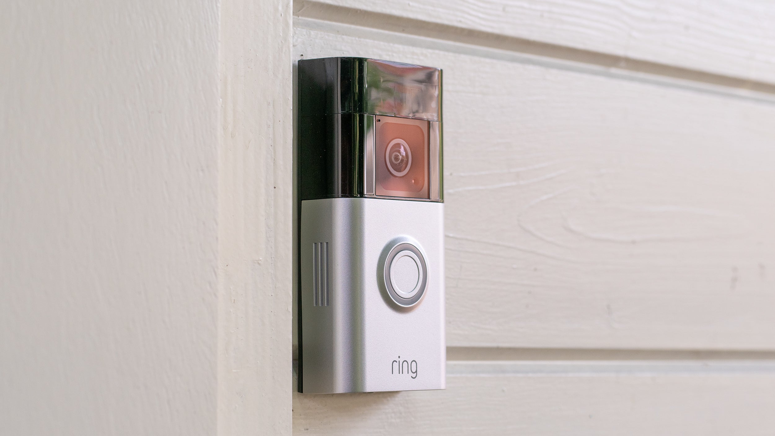 The Ring Video Doorbell Plus mounted on a white wood wall, next to a white painted front door