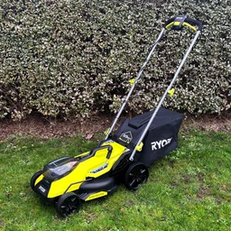 The Ryobi RY18LMX33A lawn mower on a lawn in front of a hedge