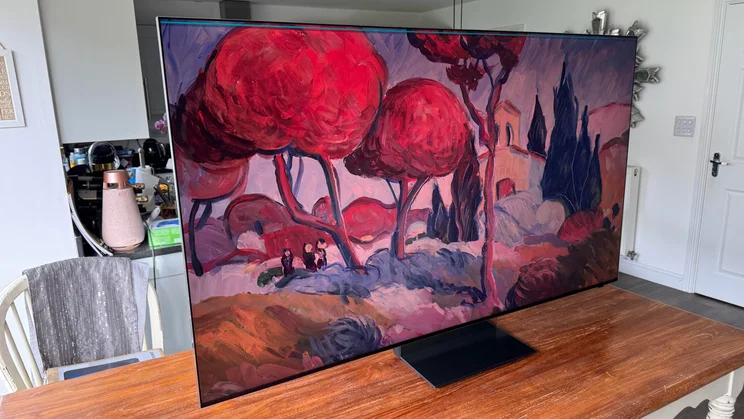 Left view of the Samsung R95H Micro LED TV on a wooden table in a conservatory displaying an impressionist digital artwork with red trees